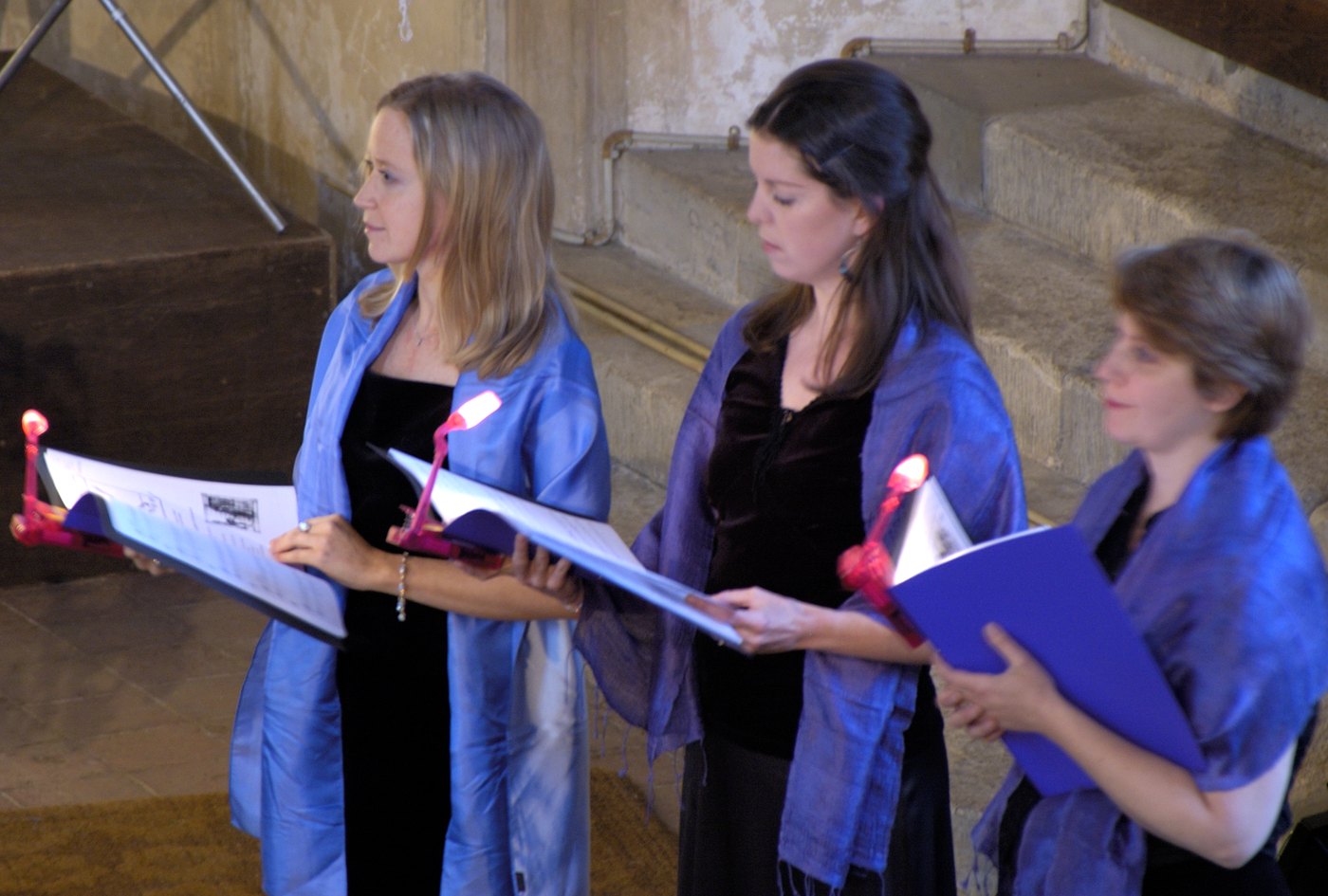 Three singers of TONUS PEREGRINUS performing with folders and reading lights